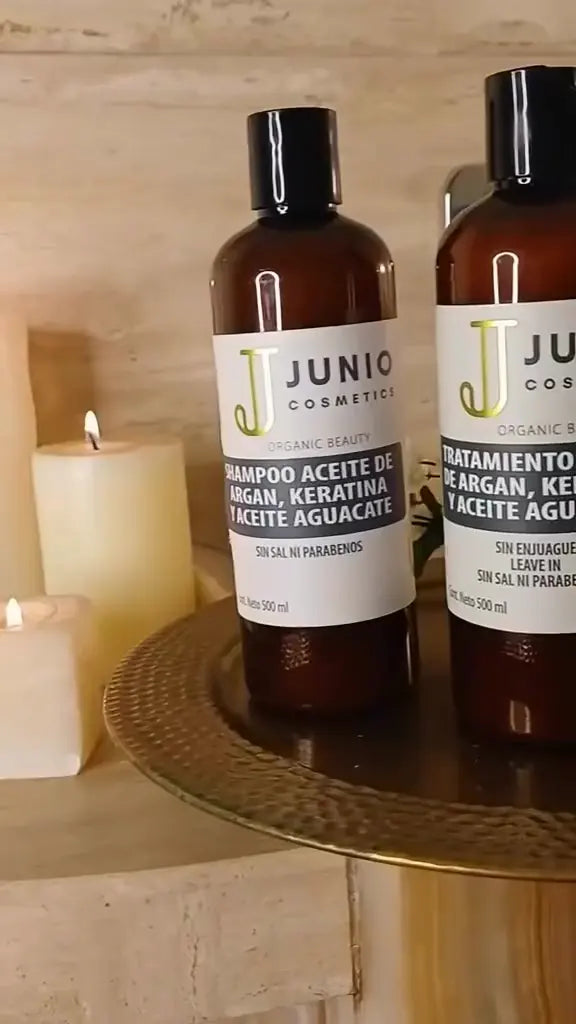 Frascos JUNIO de la línea argán, keratina y aguacate entre velas; el producto cae en la palma y se aplica en el cabello.